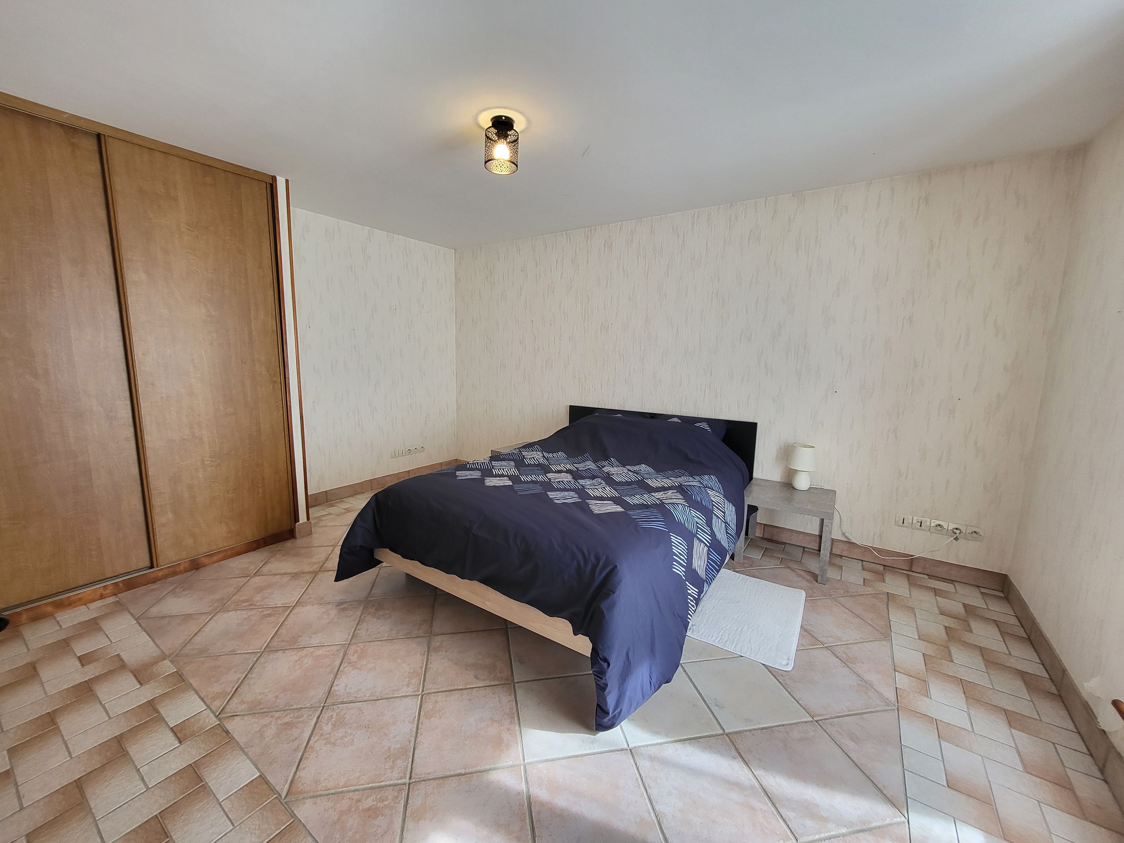 A bedroom with a bed, a nightstand, a wardrobe, and a ceiling light fixture.
