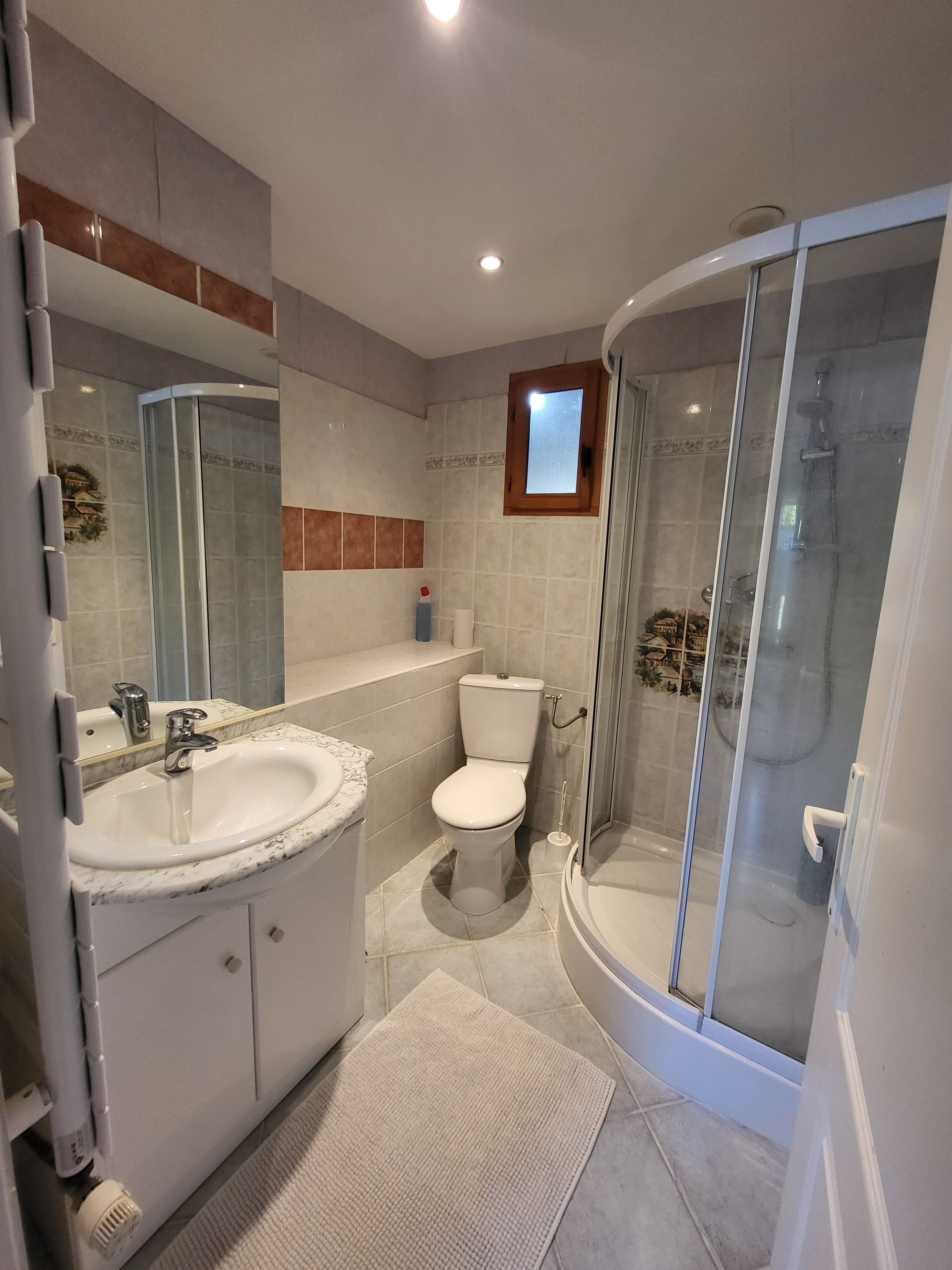 Een moderne badkamer met een douchecabine van glas, een wit wastafeltje en een toilet.