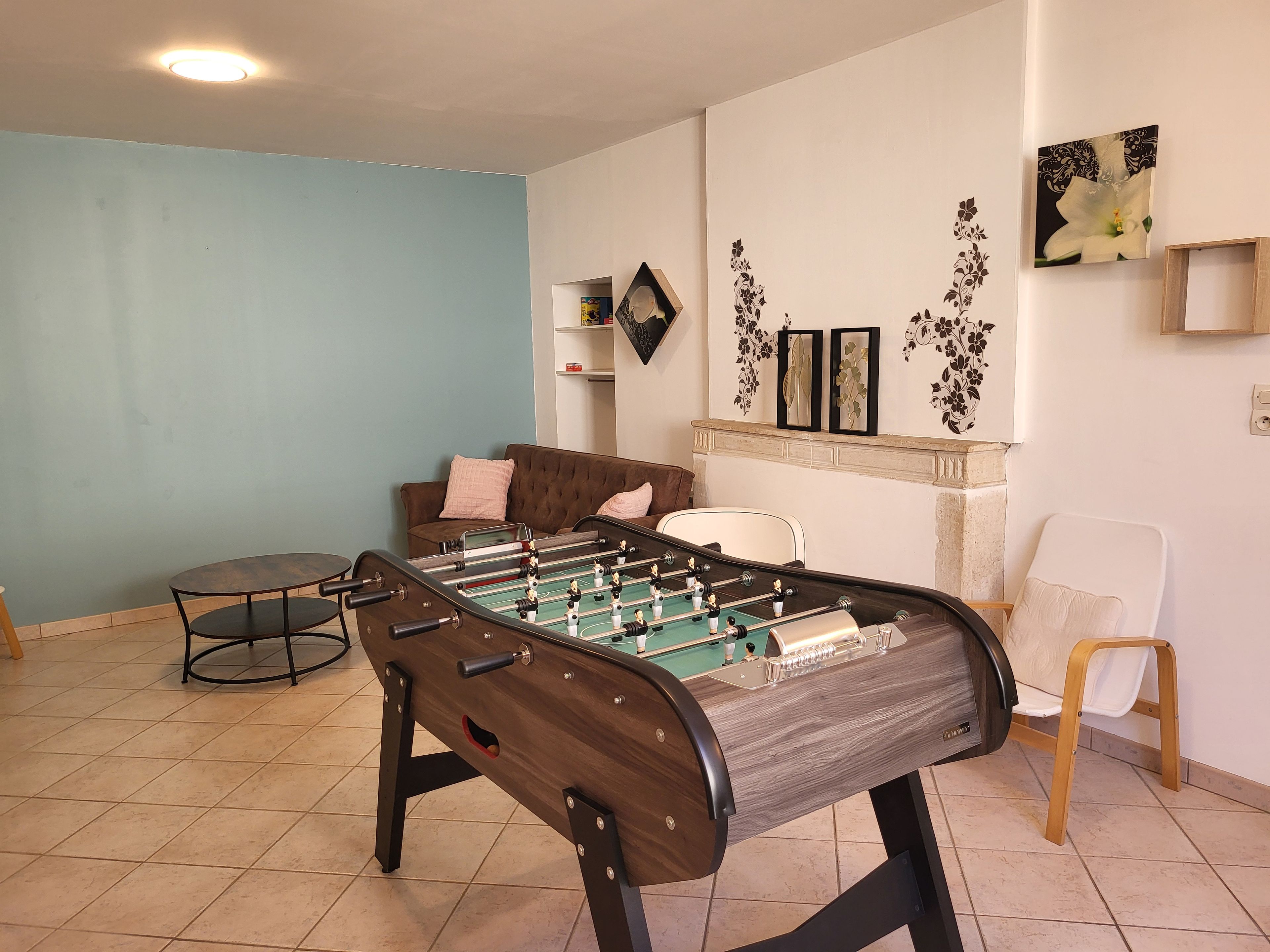 Een kamer met een tafelvoetbaltafel, een bruine bank, een witte stoel en decoratieve wandkunst.