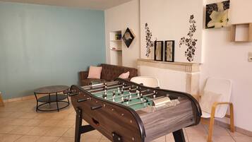 Een kamer met een tafelvoetbaltafel, een bruine bank, een witte stoel en decoratieve wandkunst.