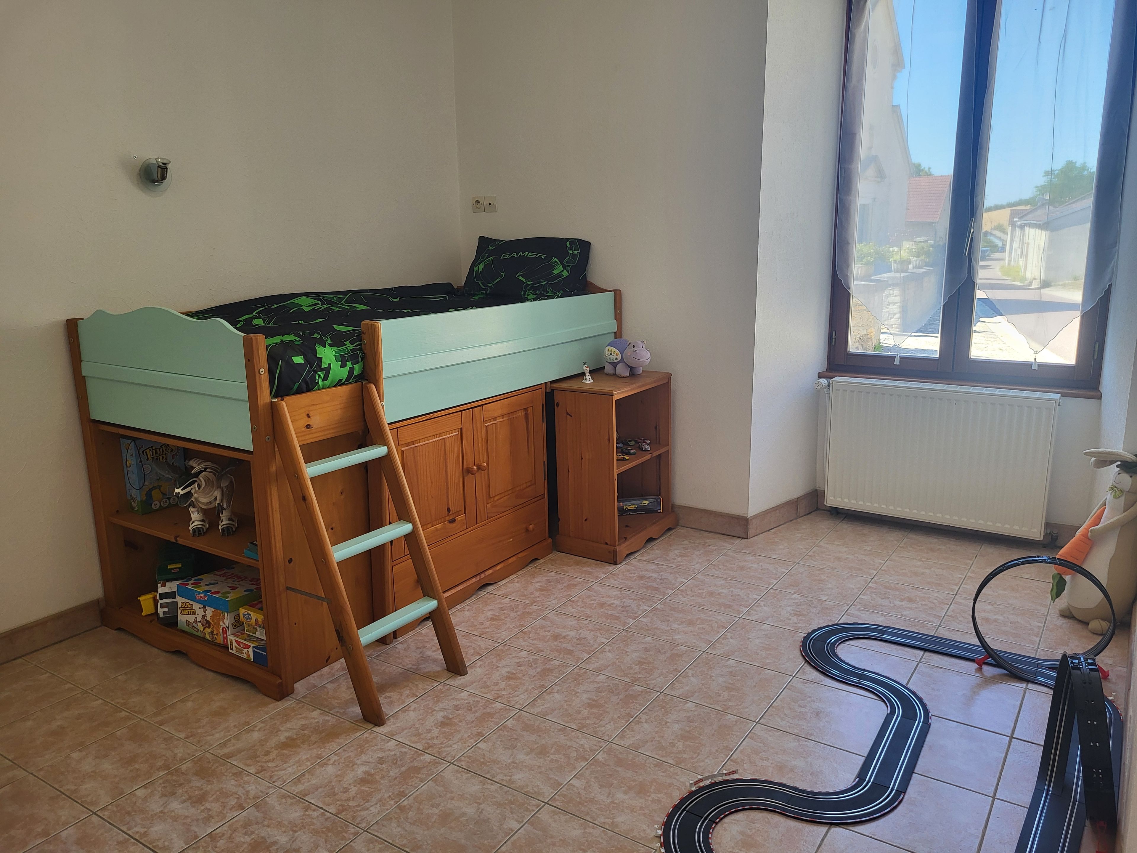 Een kinderkamer met een stapelbed, een houten ladder en een treinbaan op de vloer.
