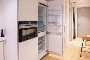 Eine moderne Küche mit Einbauofen und Kühlschrank, ausgestattet mit zahlreichen Stauräumen und einer sichtbaren Weinflasche.