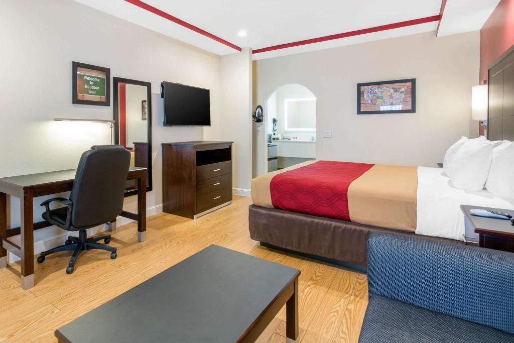 A hotel room with a bed, desk, chair, and a TV.