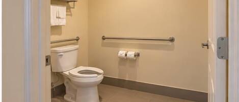 A standard hotel bathroom with a toilet, handrails, and a towel rack.