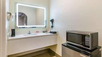 A hotel bathroom with a sink, a mirror with lights, a telephone, and a microwave.