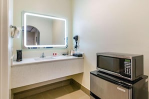 A hotel bathroom with a sink, a mirror with lights, a telephone, and a microwave.