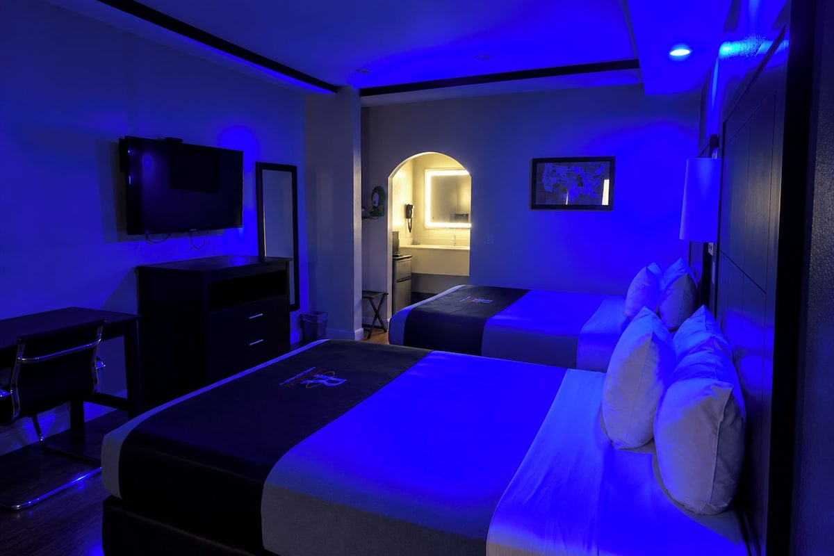 A hotel room with a bed, a desk, a chair, a television, and a bathroom visible through an archway.