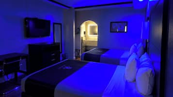 A hotel room with a bed, a desk, a chair, a television, and a bathroom visible through an archway.