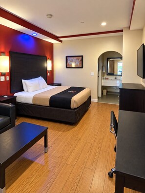 Quarto de hotel com cama, mesa de cabeceira e escrivaninha com rodízios.