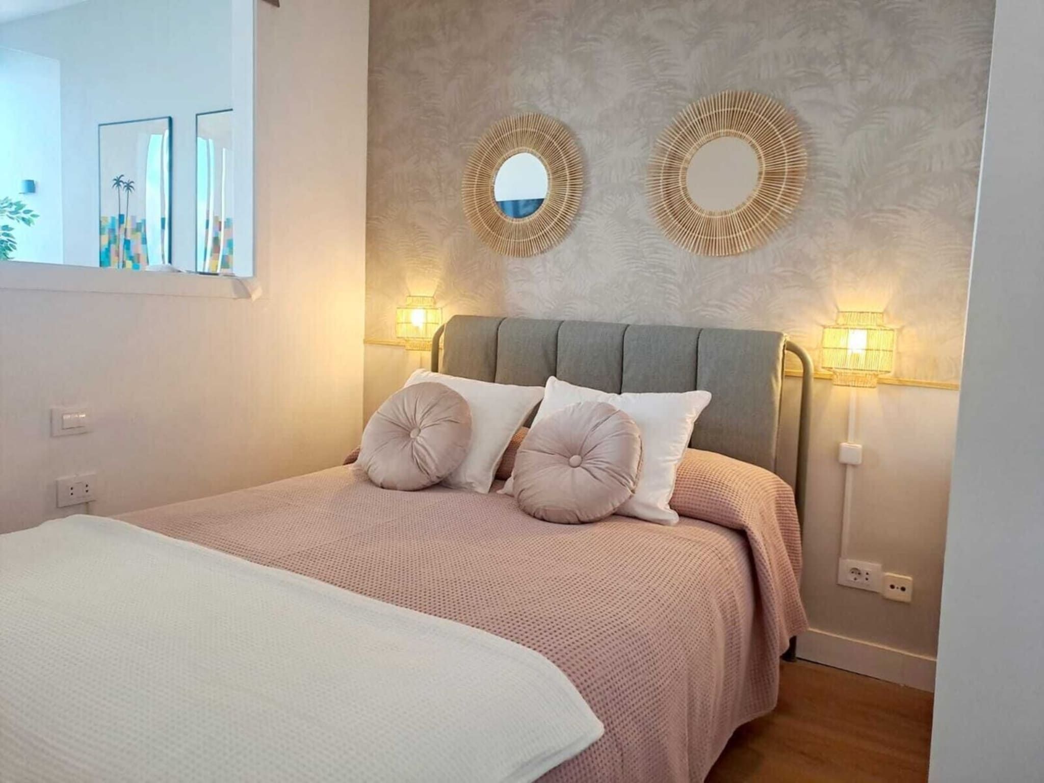 A bedroom with a bed, two wall-mounted lights, and two wall mirrors.