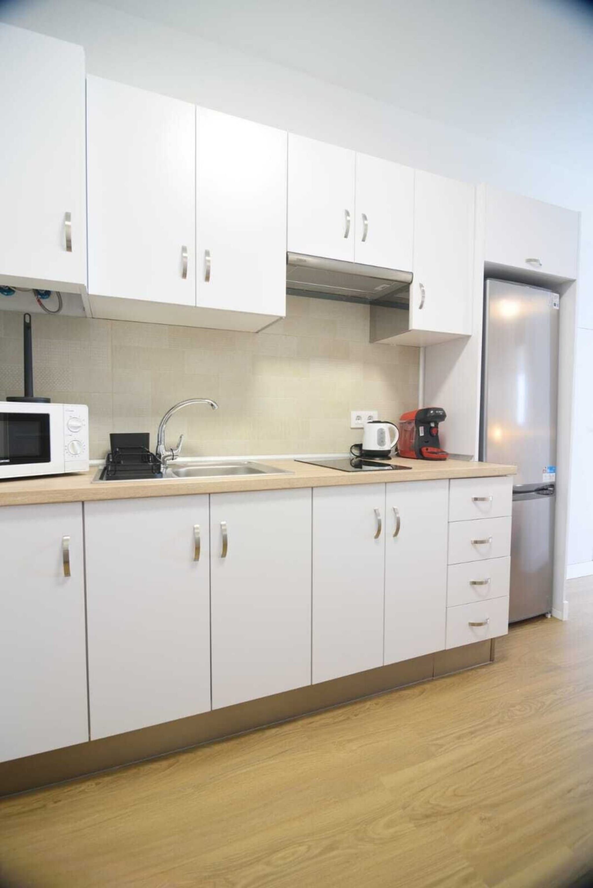 A modern kitchen with white cabinets, a stainless steel refrigerator, a microwave, and a coffee maker.