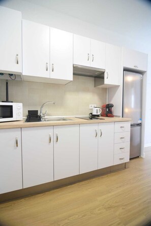 Eine moderne Küche mit weißen Schränken, einem Edelstahlkühlschrank, einer Mikrowelle und einer Kaffeemaschine.
