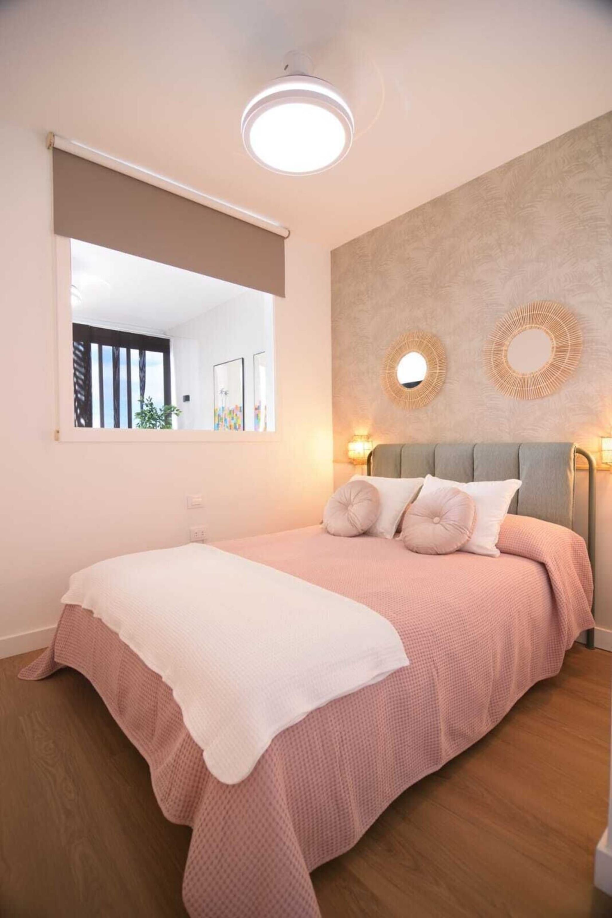 A bedroom with a bed, a large window, and a wall-mounted mirror.