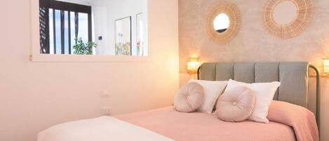 A bedroom with a bed, a large window, and a wall-mounted mirror.
