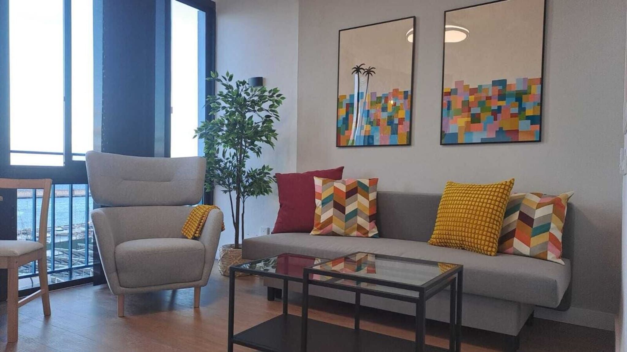 Ein Wohnzimmer mit grauem Sofa, einem Sessel, einem Couchtisch und zwei abstrakten Gemälden.