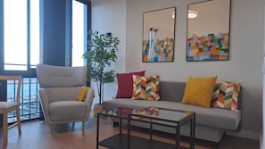 Ein Wohnzimmer mit grauem Sofa, einem Sessel, einem Couchtisch und zwei abstrakten Gemälden.