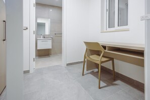 Ein Zimmer mit Schreibtisch, Stuhl und einem durch eine offene Tür einsehbaren Badezimmer.