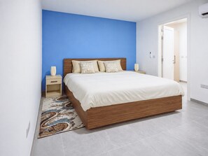A bedroom with a large bed, a nightstand, a bedside table, and a patterned rug. - Modern Maisonette with Pool in Gharghur (Ħal Għargħur)