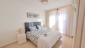 A bedroom with a bed, nightstands, a lamp, and a window with curtains. - Olivia Playa La Arena (Puerto de Santiago)
