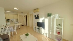 A modern living room with a flat-screen TV, a dining area with a table and chairs, and a kitchen with cabinets and appliances. - Olivia Playa La Arena (Puerto de Santiago)