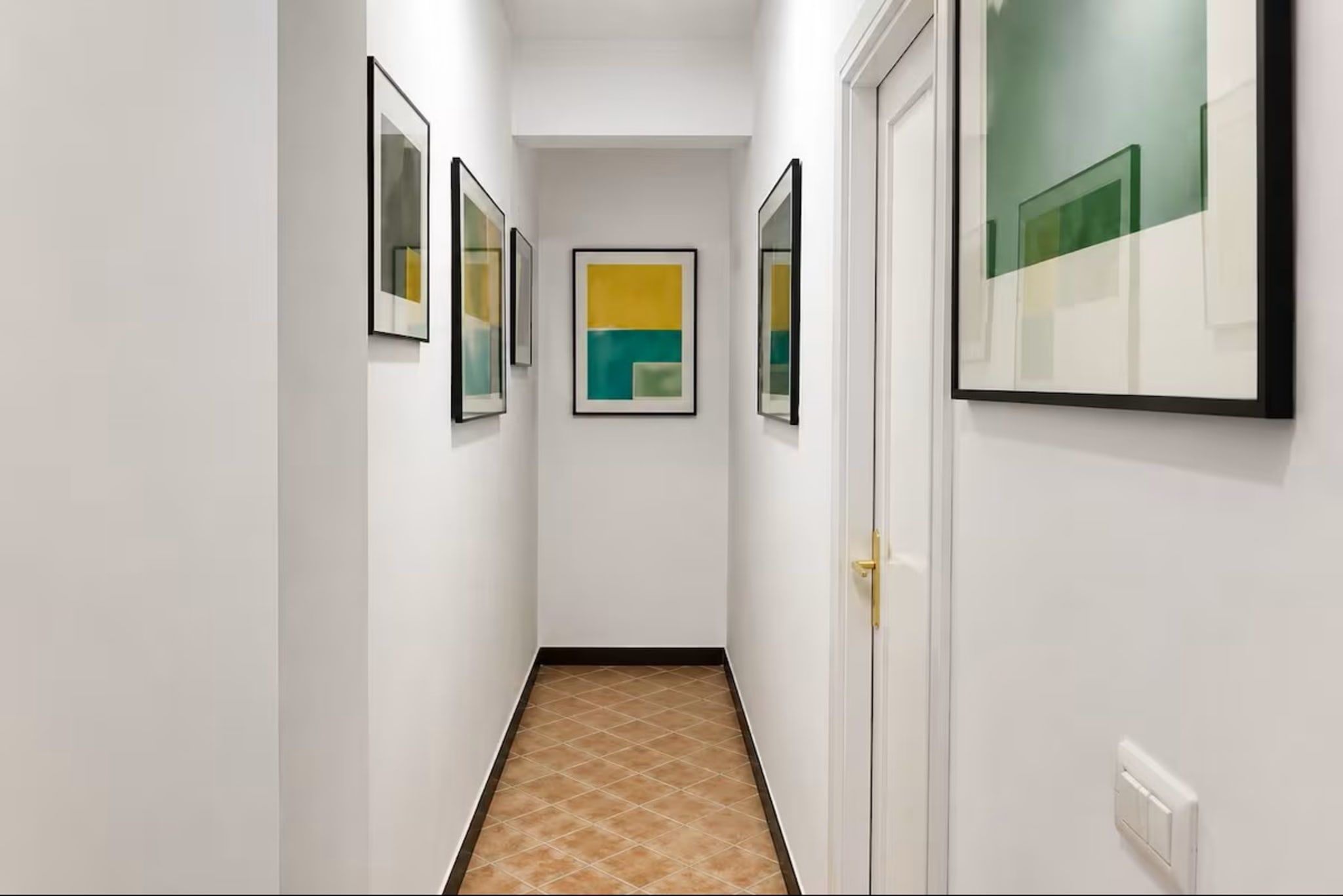 A hallway with framed artwork on the walls, a door on the right, and a tiled floor.