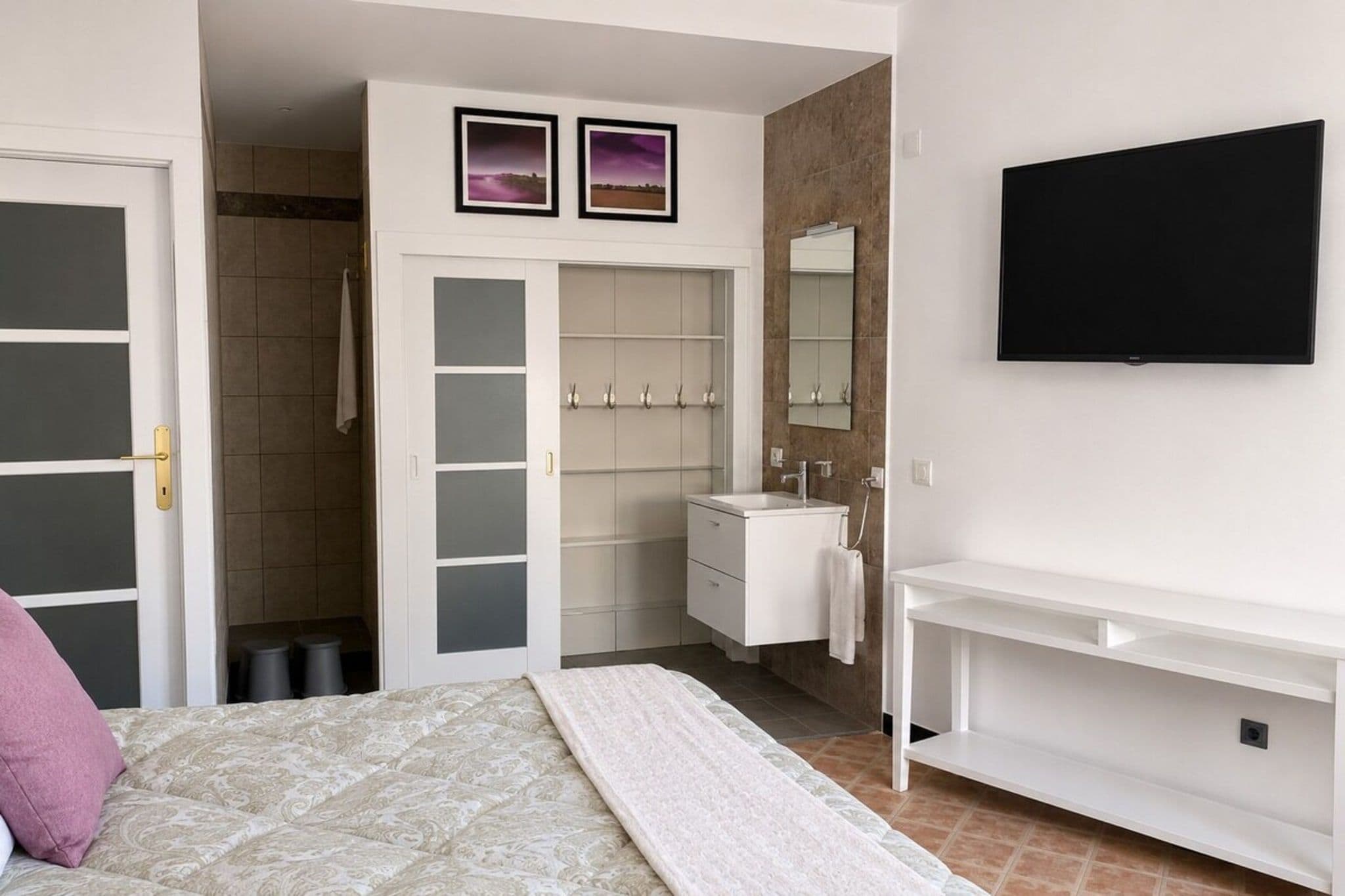 Quarto com cama, guarda-roupa, penteadeira com espelho e televisão na parede.