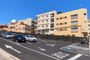 Un espace de stationnement avec plusieurs voitures, une place de stationnement réservée aux personnes handicapées et un immeuble à étages doté de balcons.