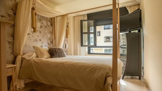 Een slaapkamer met een bed, gordijnen, een televisie en uitzicht.