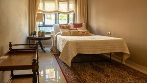 Een slaapkamer met een bed, een stoel, een tafeltje en een raam met gordijnen.