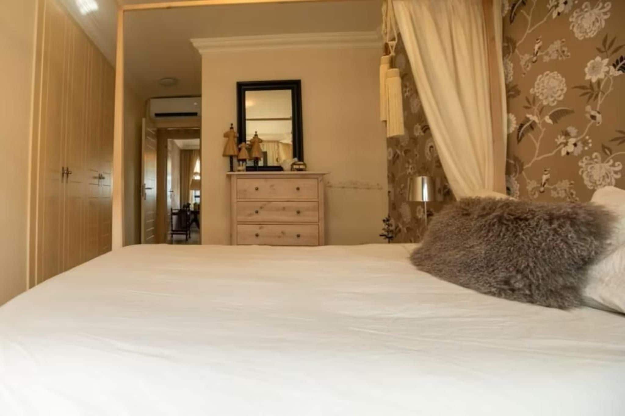 Une chambre à coucher avec un lit, une commode, un miroir et un papier peint à motifs floraux.