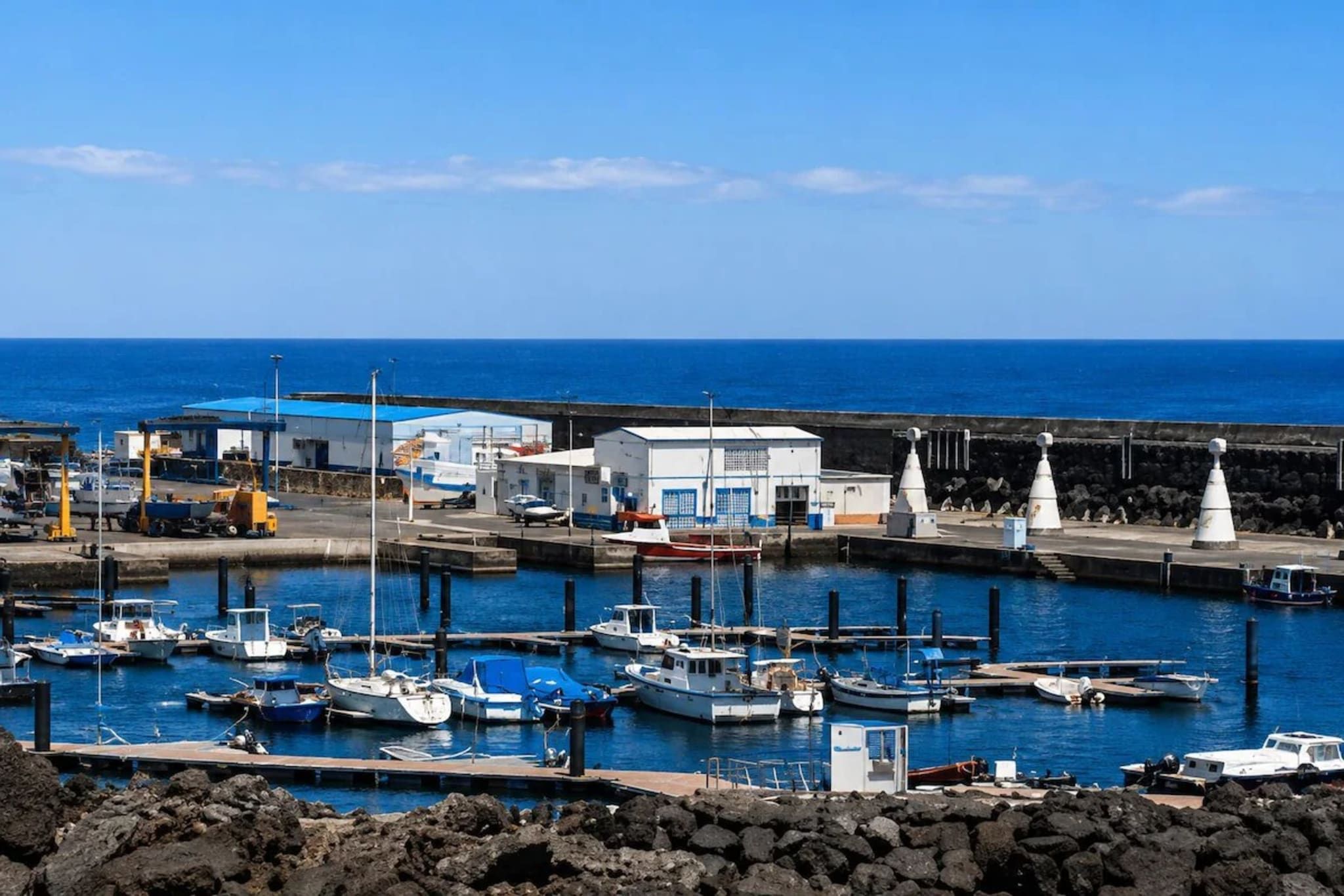 Un puerto deportivo con barcos amarrados, un edificio con techo azul y un cielo azul despejado.