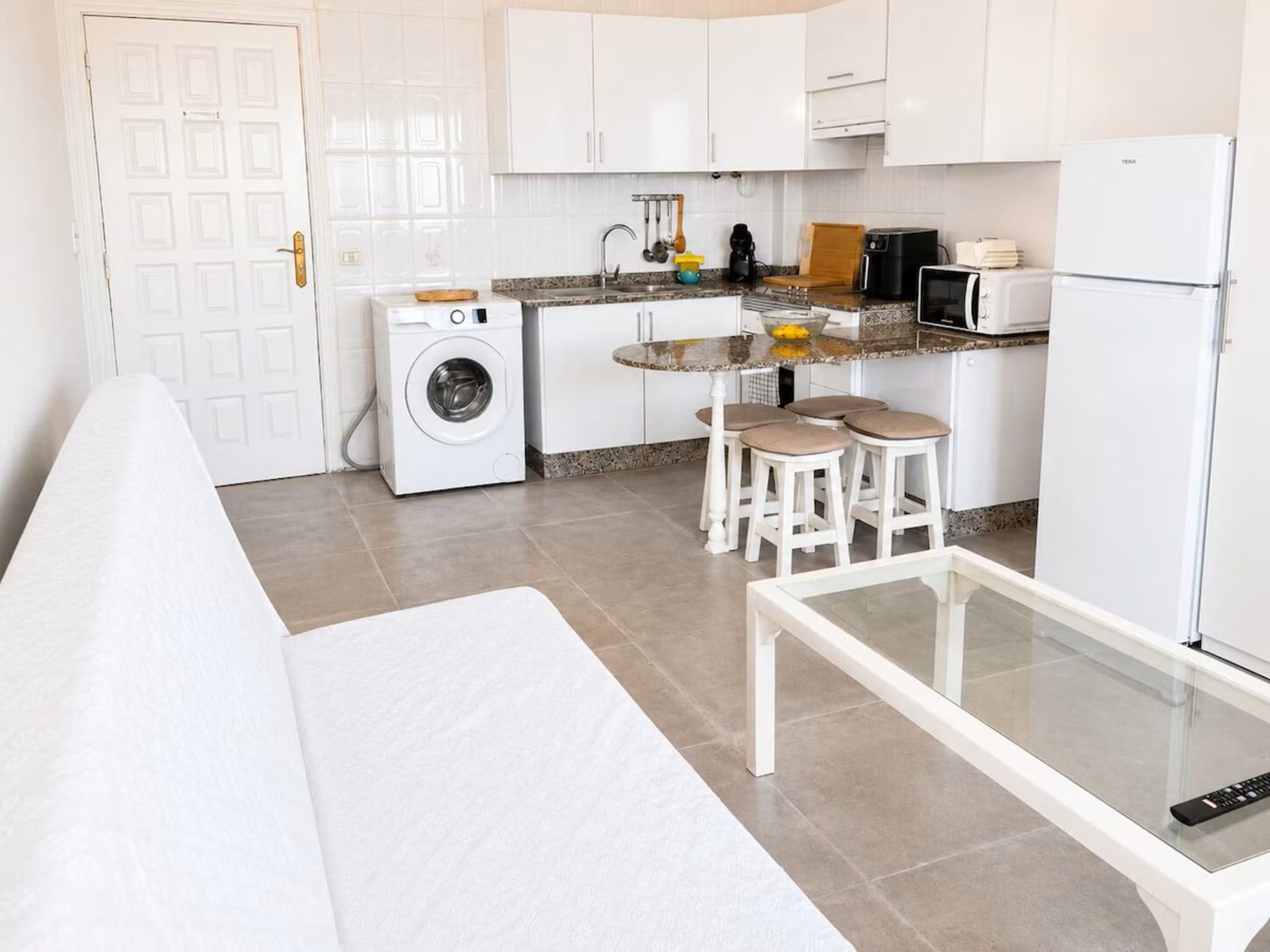 A compact kitchen with a washing machine, a dining area with a table and stools, and a refrigerator.