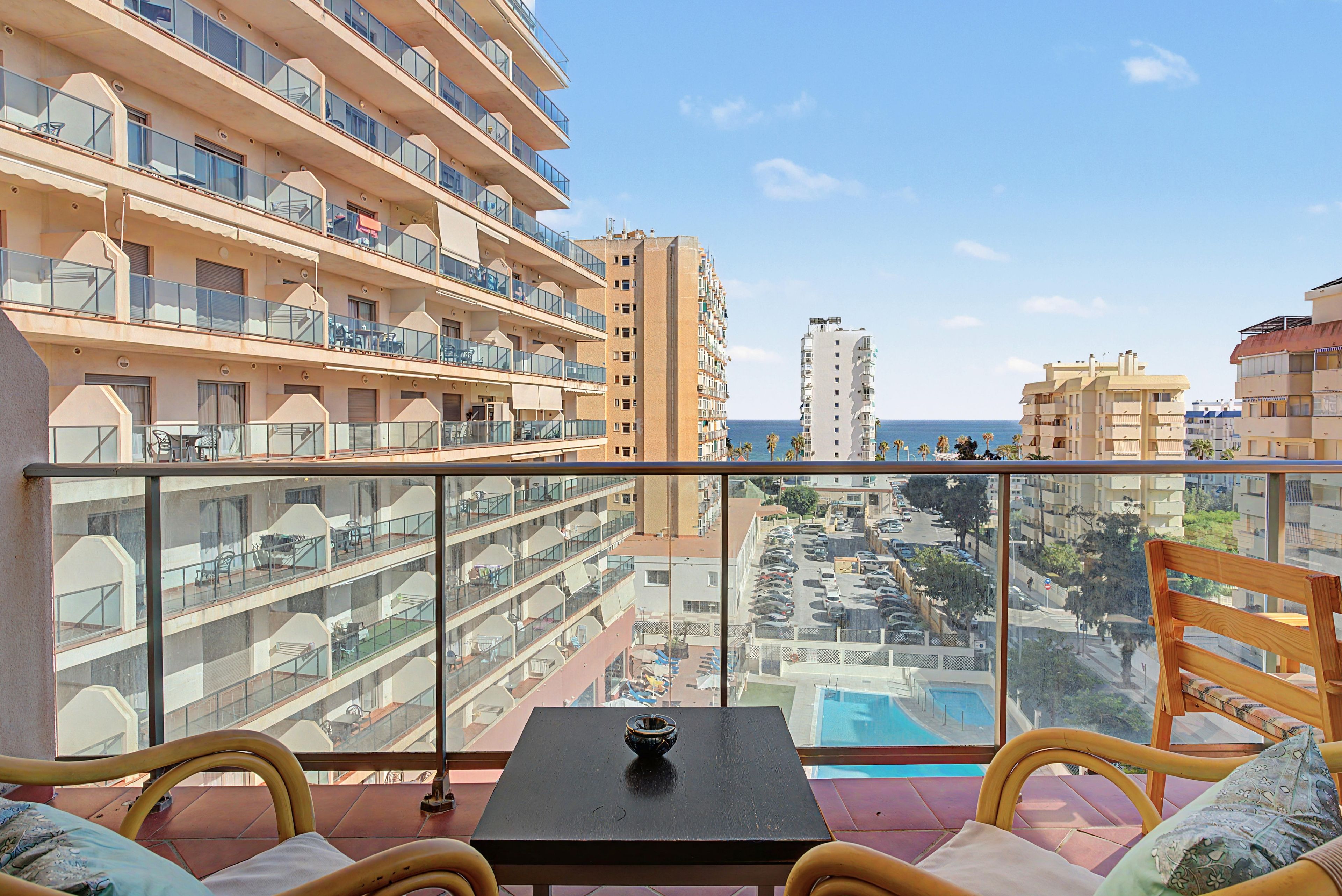 Varanda com mesa e cadeiras, vista para um horizonte urbano com vários edifícios e céu claro.