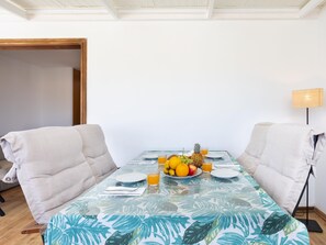 A dining area with a table set for two, featuring a tropical leaf tablecloth, a fruit bowl with oranges, lemons, and a pineapple, and a glass of orange juice. - CHL Casa Arthur, ático en El Médano cerca de la pl (El Médano)