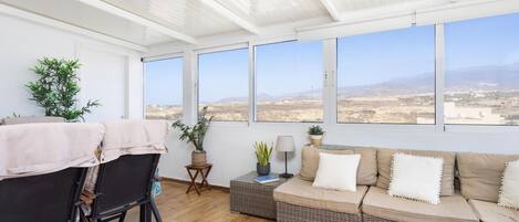 Una habitación soleada con sofá, sillas y vistas a un paisaje desértico a través de amplios ventanales.