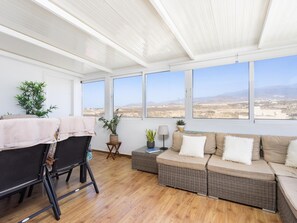 A sunlit room with a sofa, chairs, and a view of a desert landscape through large windows. - CHL Casa Arthur, ático en El Médano cerca de la pl (El Médano)