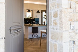 Ein Blick in eine moderne Küche mit Essbereich, mit Pendelleuchten, einem Holztisch und einem schwarzen Stuhl.