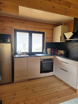 A compact kitchen with wooden cabinets, a built-in oven, a microwave, and a window with blinds.