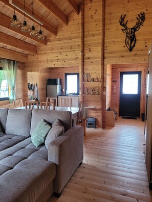 A wooden interior with a sofa, dining table, kitchen area, and a deer head decoration.