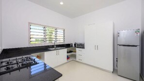 A kitchen with a gas stove, white cabinets, a refrigerator, and a window with blinds.