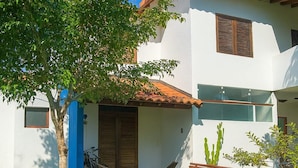 A two-story house with a tiled roof, a front porch with a bench, and a cactus plant in the yard. - Maria Ines Bondesan (ubatuba)