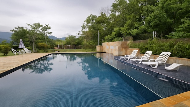 A rectangular swimming pool with clear blue water, surrounded by a stone deck and white lounge chairs. - Maria Ines Bondesan (ubatuba)