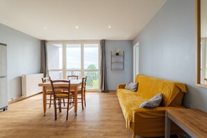 Un salon moderne avec une table à manger en bois, des chaises, un canapé et un balcon offrant une vue agréable.