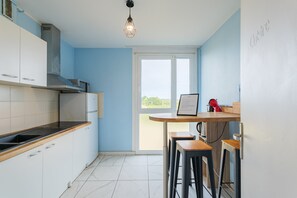 Une cuisine moderne avec des armoires blanches, une hotte de cuisinière en acier inoxydable, un four à micro-ondes et une cuisinière à gaz. On y trouve un comptoir-bar en bois avec des tabourets et un menu encadré accroché au mur.