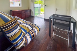 A room with a striped sofa, a small table, and a door leading to an outdoor area. - L'Oasis dans le Désert - à 350 m de la plage (Sainte-Luce)