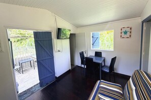 A room with a dining table and chairs, a television mounted on the wall, and a window with shutters. - L'Oasis dans le Désert - à 350 m de la plage (Sainte-Luce)