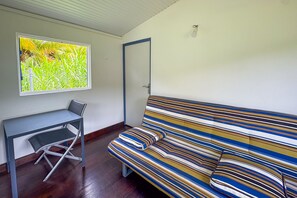 A room with a striped sofa, a small desk with a chair, and a window with a view of greenery. - L'Oasis dans le Désert - à 350 m de la plage (Sainte-Luce)