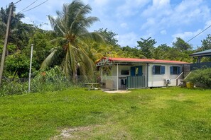 Une petite maison avec un toit rouge, entourée d’une végétation luxuriante et d’un palmier.