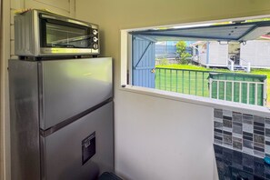 Une cuisine compacte dotée d’un four et d’un micro-ondes intégrés, d’une petite fenêtre donnant sur une cour verdoyante et d’un pare-feu en carrelage.