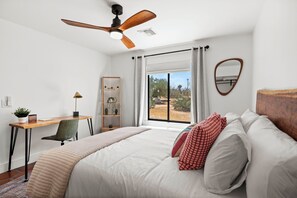 A bedroom with a bed, a desk, a chair, a ceiling fan, and a window with curtains. - Desert Shadow A 10ac Retreat w/Pool + Hot Tub+ Pickleball + Archery + More (Yucca Valley)